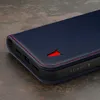 A close-up shot of a dark blue leather phone case with red stitching and a red bull logo. Produktbild-Vorschau