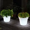 Two illuminated LED solar flower pots with plants on a wooden deck at night. Produktbild-Vorschau