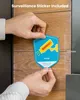 A person is holding a surveillance sticker to a wooden surface. Produktbild-Vorschau