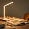 A white LED desk lamp is illuminating an open book on a wooden table. Produktbild-Vorschau