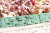 A green garden border with a brick pattern is placed in front of plants with red and brown leaves. Produktbild-Vorschau