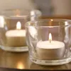 Two lit tea lights in glass holders on a reflective surface. Voir les images du produit