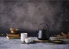 A tea set with a teapot, cups, and books on a textured surface. Voir les images du produit