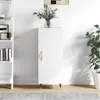 A white cabinet with a gold handle stands against a white wall, next to a bookshelf and a potted plant. Produktbild-Vorschau