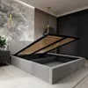 A modern bedroom with a grey upholstered bed frame, its storage compartment open, revealing the wooden slats of the mattress base. The room features a large mural on the wall and dark wooden wardrobes. Náhled obrázku produktu