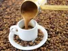 Coffee being poured from a cezve into a small white cup, surrounded by coffee beans. Anteprima dell’immagine prodotto