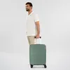 A man is standing and holding the handle of a green suitcase. Podgląd zdjęcia produktu