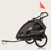 A gray and black child trailer for bicycles or as a stroller, with a red flag on top. Produktbild-Vorschau