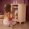 A young girl is playing with a wooden doll wardrobe, organizing clothes for her dolls. Produktbild-Vorschau