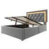 A grey upholstered bed frame with the mattress support mechanism open, revealing storage space underneath. The headboard has tufted detailing and integrated LED lighting. Náhľad obrázku produktu