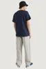 A person wearing a navy blue t-shirt and light gray jeans, viewed from the back. Voir les images du produit