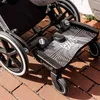 A close-up view of a Lascal Buggy Board Maxi attached to a stroller, shown on a brick pathway. Náhled obrázku produktu