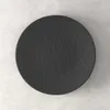A dark gray, round plate with a textured surface is shown from a top-down perspective on a light gray and white speckled background. Podgląd zdjęcia produktu