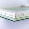 A close-up shot of the edge of a rectangular mirror with LED lights attached to its frame, resting on a glass surface. Produktbild-Vorschau