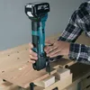 A person is using a Makita cordless oscillating multi-tool to cut into a piece of wood on a workbench. Produktbild-Vorschau