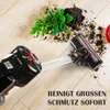 A cordless stick vacuum cleaner is shown cleaning up dirt and a small plant from a wooden floor. Produktbild-Vorschau