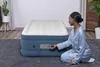 A woman is kneeling next to an inflatable mattress and adjusting its controls. Náhled obrázku produktu