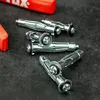 Several metal hollow wall anchors are scattered on a dark textured surface, with parts of red plastic tools in the background. Náhled obrázku produktu