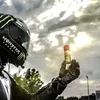 A person in motorcycle gear holds up a spray can against a cloudy sky. Produktbild-Vorschau