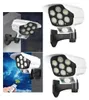 Vier Ansichten einer weißen Solar-Sicherheitsleuchte mit schwarzer Montagehalterung und mehreren LED-Lampen, eine zeigt eine Hand, die eine Fernbedienung hält Voir les images du produit