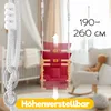A baby swing is shown in a nursery setting, with a crib in the background and a rocking chair with a teddy bear to the side. The swing is red with wooden accents and white ropes. Produktbild-Vorschau