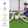 A woman is interacting with a pool filter system set up on a grassy area, likely for a swimming pool. Produktbild-Vorschau