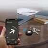 A hand holding a smartphone displaying a key finder app, with a set of keys and an Apple AirTag on a wooden desk next to a laptop and books. Produktbild-Vorschau