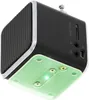 A close-up, angled view of a small, black, cube-shaped portable speaker with a silver trim. The speaker has a mesh grille on one side and various ports and a micro SD card slot on another. The bottom of the speaker has a light green plastic plate with scre Náhľad obrázku produktu