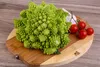 A Romanesco broccoli with cherry tomatoes and garlic on a wooden cutting board. Voir les images du produit