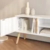 A white TV stand with an open cabinet door, showing books inside and two decorative vases on top. Voir les images du produit