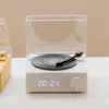 A white Bluetooth speaker designed to look like a vintage record player sits on a white surface, with a clear plastic lid open. A second yellow device is partially visible to the left. Podgląd zdjęcia produktu