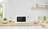 A white Panasonic microwave is displayed on a kitchen counter with some food items and kitchen utensils. Voir les images du produit