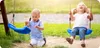 Two young children are playing on swings in an outdoor playground on a sunny day. Anteprima dell’immagine prodotto