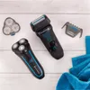 Two electric shavers and accessories are laid out on a light wooden surface, with blue towels in the background. Anteprima dell’immagine prodotto