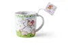 A white mug with a cartoon sheep design and a tag attached to the handle. Náhled obrázku produktu
