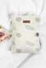 A cream-colored organizer bag with a leaf pattern, lying on a white fluffy surface. Produktbild-Vorschau
