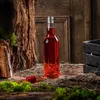A bottle of red liquid sits on a rustic wooden surface, surrounded by moss and straw, with a wooden crate in the background. Produktbild-Vorschau