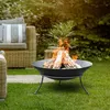 A fire pit with burning logs in a garden setting, next to outdoor furniture. Produktbild-Vorschau