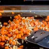 Chopped carrots and other vegetables are being cooked on a flat-top grill. Produktbild-Vorschau