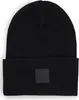 A black beanie hat with a black square logo patch on the front. Voir les images du produit