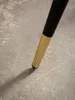 A close-up shot of a table leg with a black upper section and a gold lower section, resting on a concrete floor. Produktbild-Vorschau