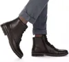 A close-up shot of a person wearing black leather boots and blue pants. Produktbild-Vorschau