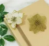 Two artificial poinsettia flowers, one white with gold trim and one gold, are placed on a brown gift box tied with twine. Green leaves are visible on the left side of the image. Podgląd zdjęcia produktu