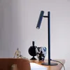 A black desk lamp is shown on a wooden desk with decorative objects. Produktbild-Vorschau
