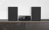 A stereo system with two speakers and a central unit is displayed on a dark countertop against a white wall. Podgląd zdjęcia produktu