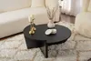 A black, modern, round coffee table is placed on a cream and brown patterned shag rug, in front of a cream sofa. A white vase with dried flowers and a small white lidded dish are on the table, along with a gold candlestick with two white candles. Produktbild-Vorschau