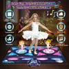 A young girl in a white ballet outfit is dancing on a colorful dance mat with animated graphics and musical notes surrounding her. Two cartoon characters are also on the mat. Produktbild-Vorschau