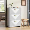 A white shoe cabinet with three drawers and gold handles is shown in a hallway next to a wooden stool. A doorway leads to a dining area with a table and chairs. Podgląd zdjęcia produktu