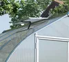 Close-up view of a greenhouse roof with an open vent, showing the aluminum frame and polycarbonate panels. Trees and a house roof are visible in the background. Náhled obrázku produktu