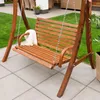A wooden garden swing seat with a white blanket draped over the armrest, placed on a paved patio next to a lawn. Náhled obrázku produktu